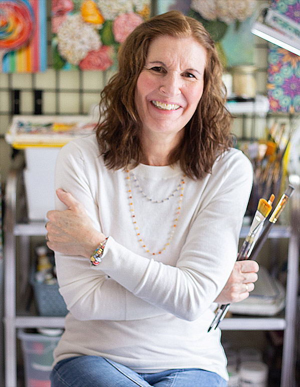 a smiling woman is holding painting brushes